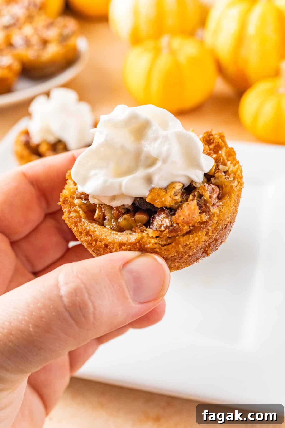 holding a mini pecan pie tart topped with whipped cream.
