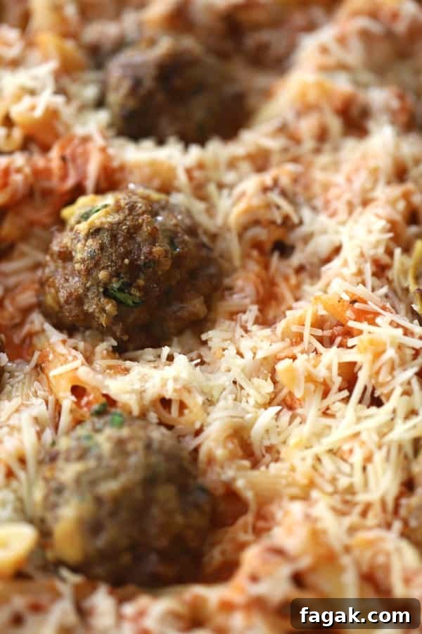 Baked penne pasta with meatballs in a baking dish topped with shredded cheese.