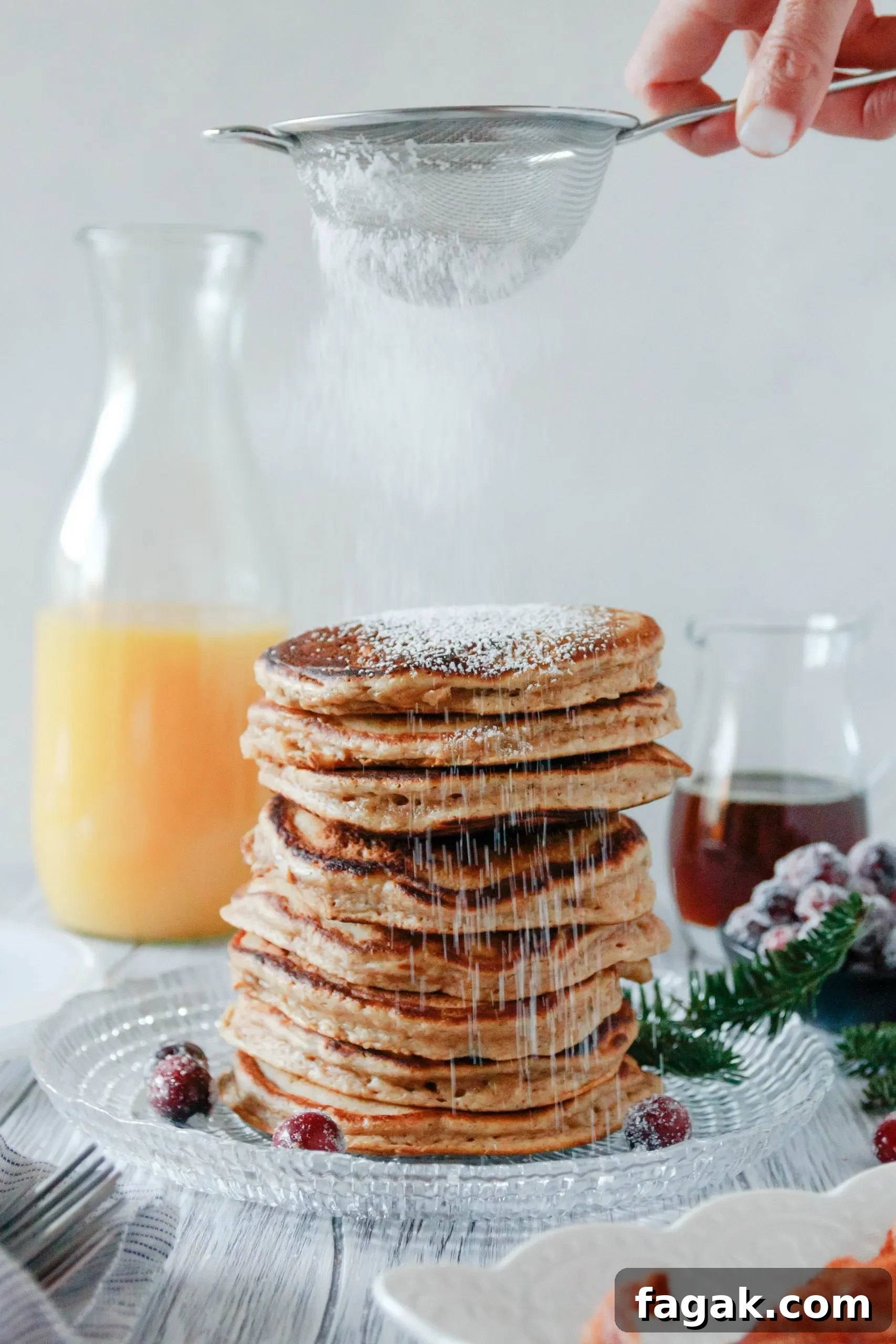small sieve with powdered sugar dusting a big stack of pancakes ready to serve!