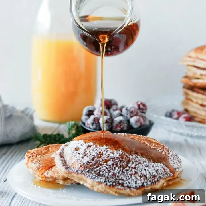 a glass pitcher pouring syrup on plated eggnog pancakes. Orange juice in the background