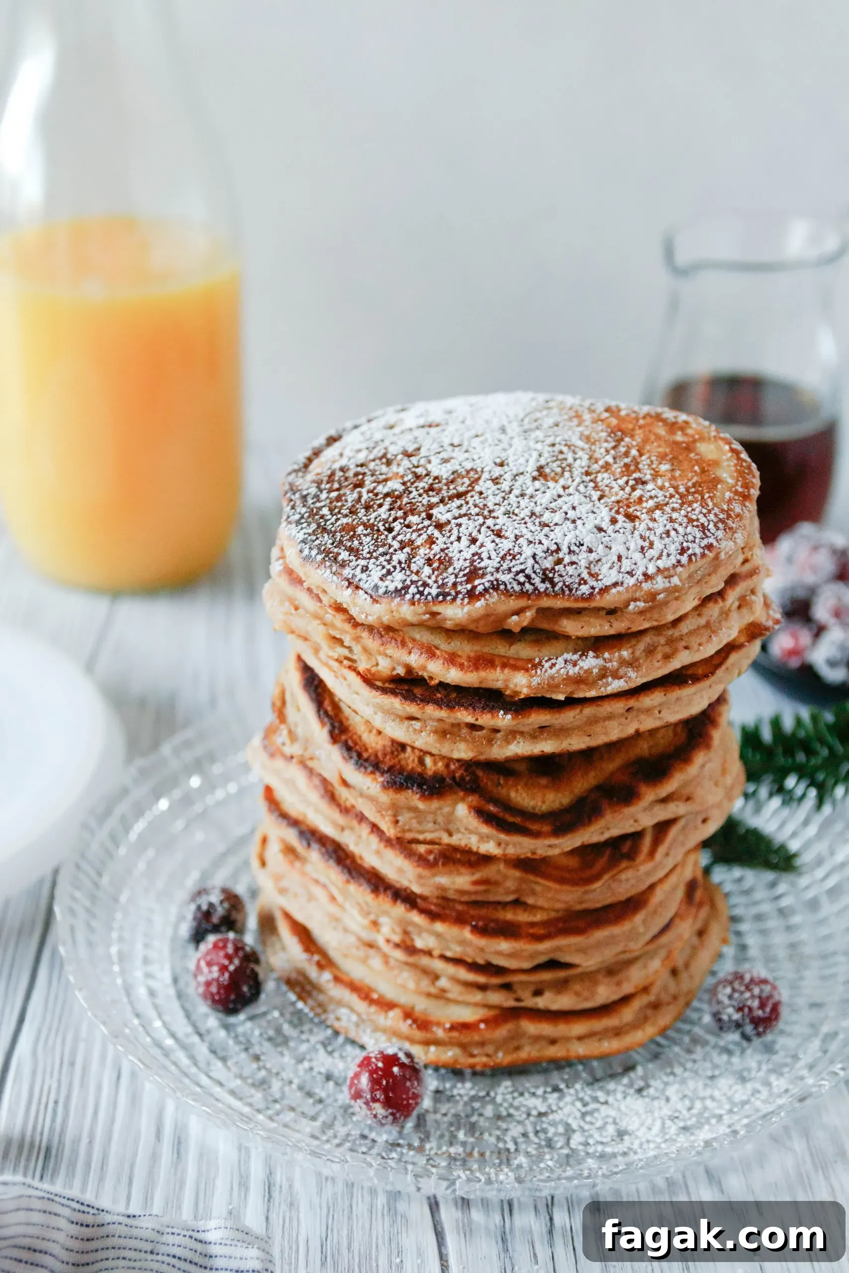 angled picture of a big stack of pancakes dusted with powdered sugar. Pancakes are on a glass plate and garnished with a few sugared cranberries.