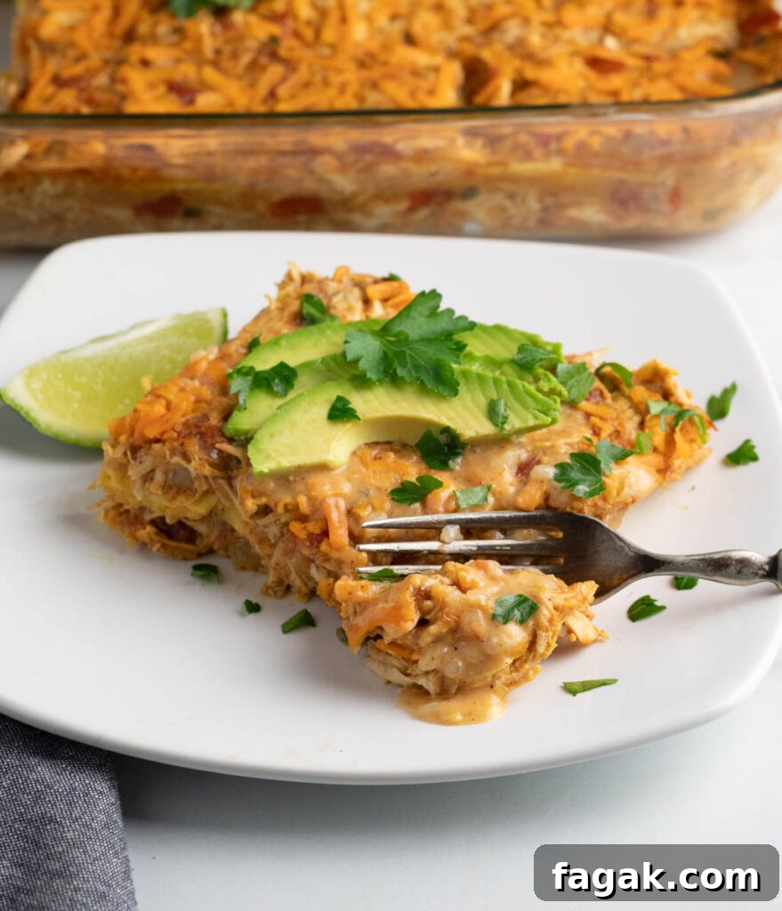 A piece of dairy free chicken casserole (King Ranch style) on a white plate with a fork cutting into the first bite and the whole casserole dish behind it.