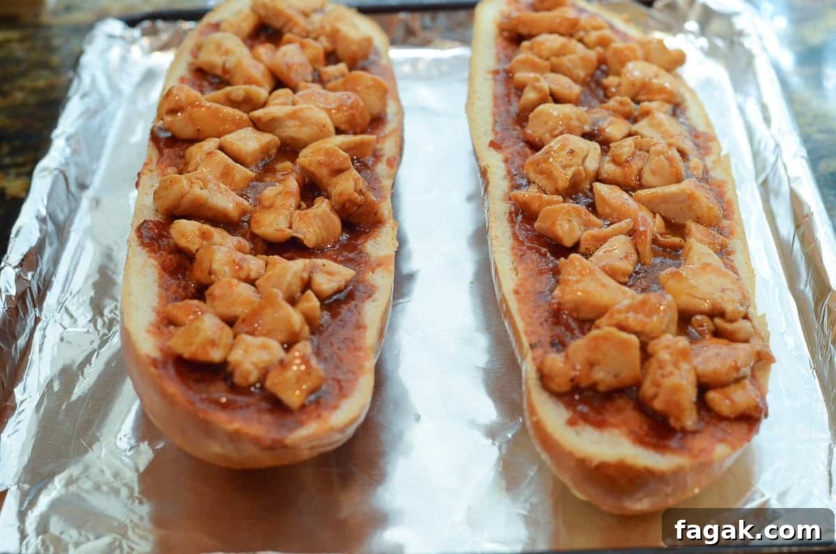 Two halves of a loaf of French bread coated with sauce and topped with chicken in BBQ sauce.