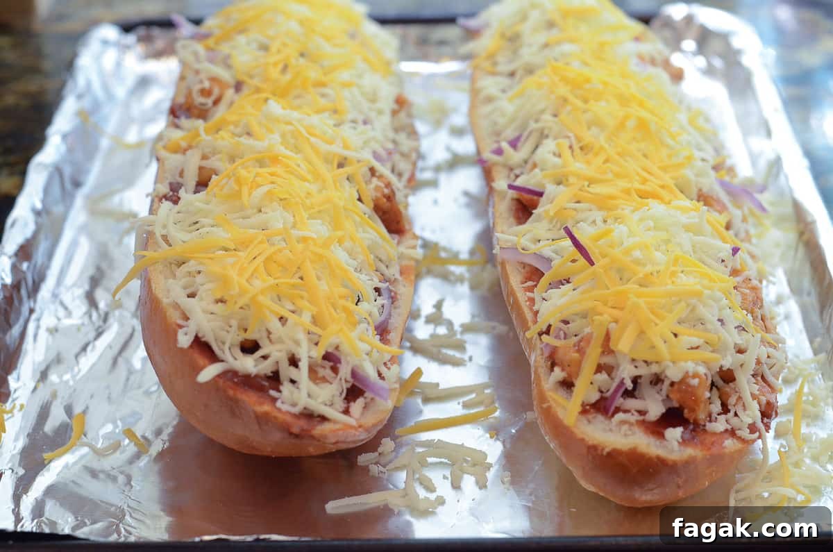 Shredded cheese on top of BBQ Chicken French Bread Pizza on a foil lined baking sheet.