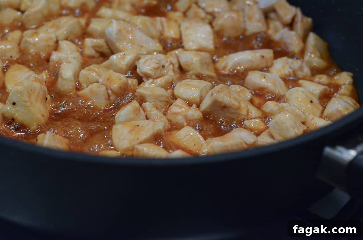 Pieces of chicken simmering in BBQ sauce in a skillet.