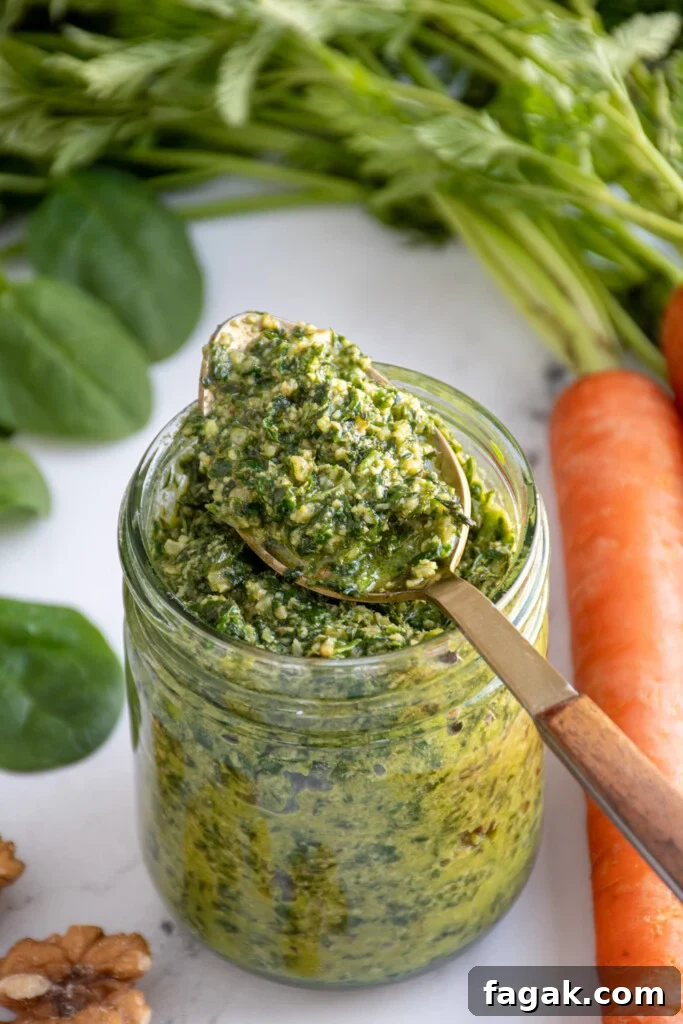 A glass jar with a spoon resting on top filled with bright green carrot top pesto.