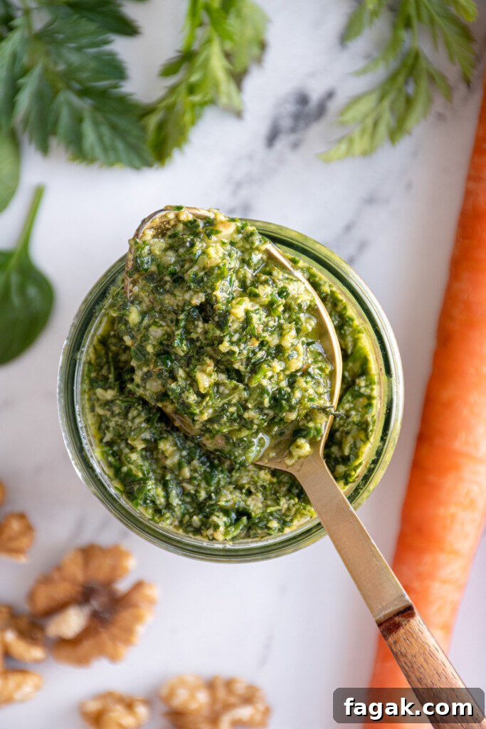 Overhead look at a glass jar with a spoon resting on the top filled with carrot top pesto.
