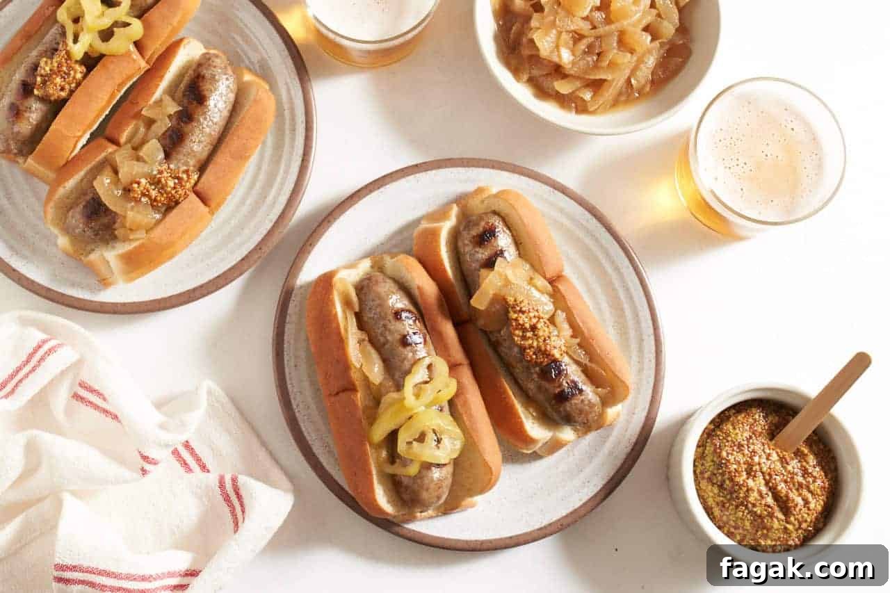 Two plates with beer brats in buns topped with onions, peppers, and mustard, two beers and small bowls of grainy mustard and onions are on the right.