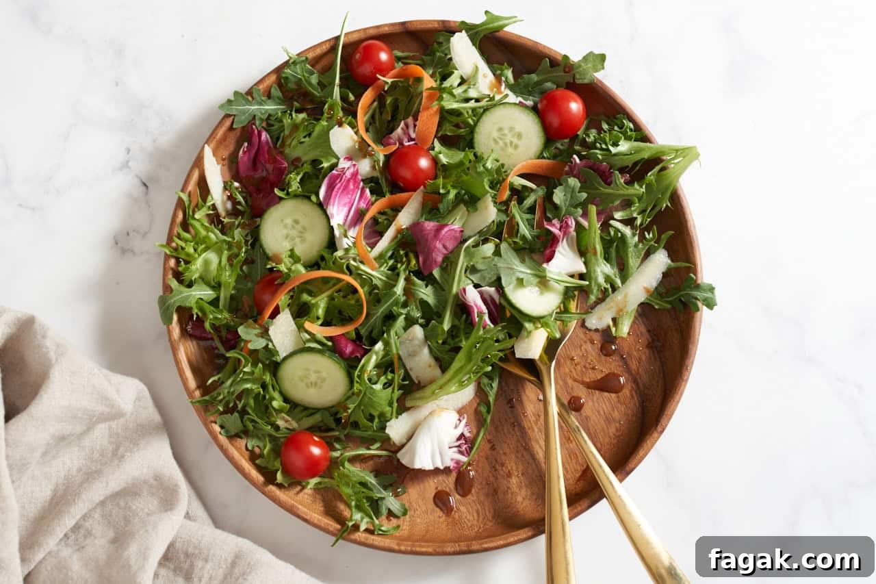 An insalata mista (Italian mixed salad) on a wooden plate with gold serving utensils.