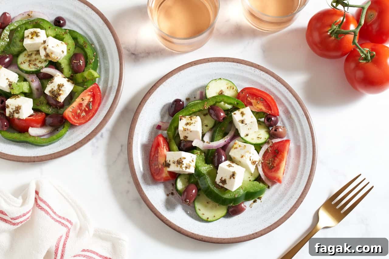 Two plates of traditional Greek salad surrounded by two glasses of wine.