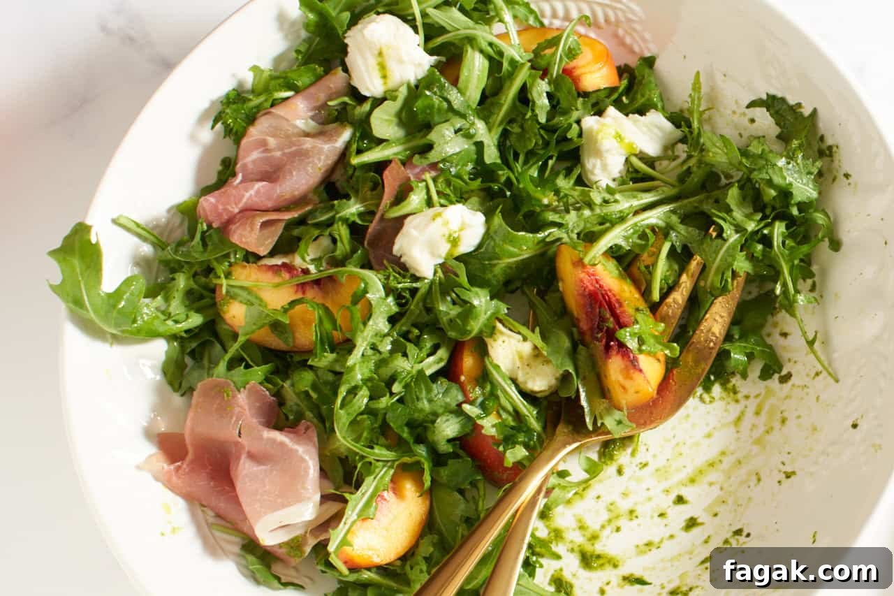 Peach salad in a white bowl with gold serving utensils in it.