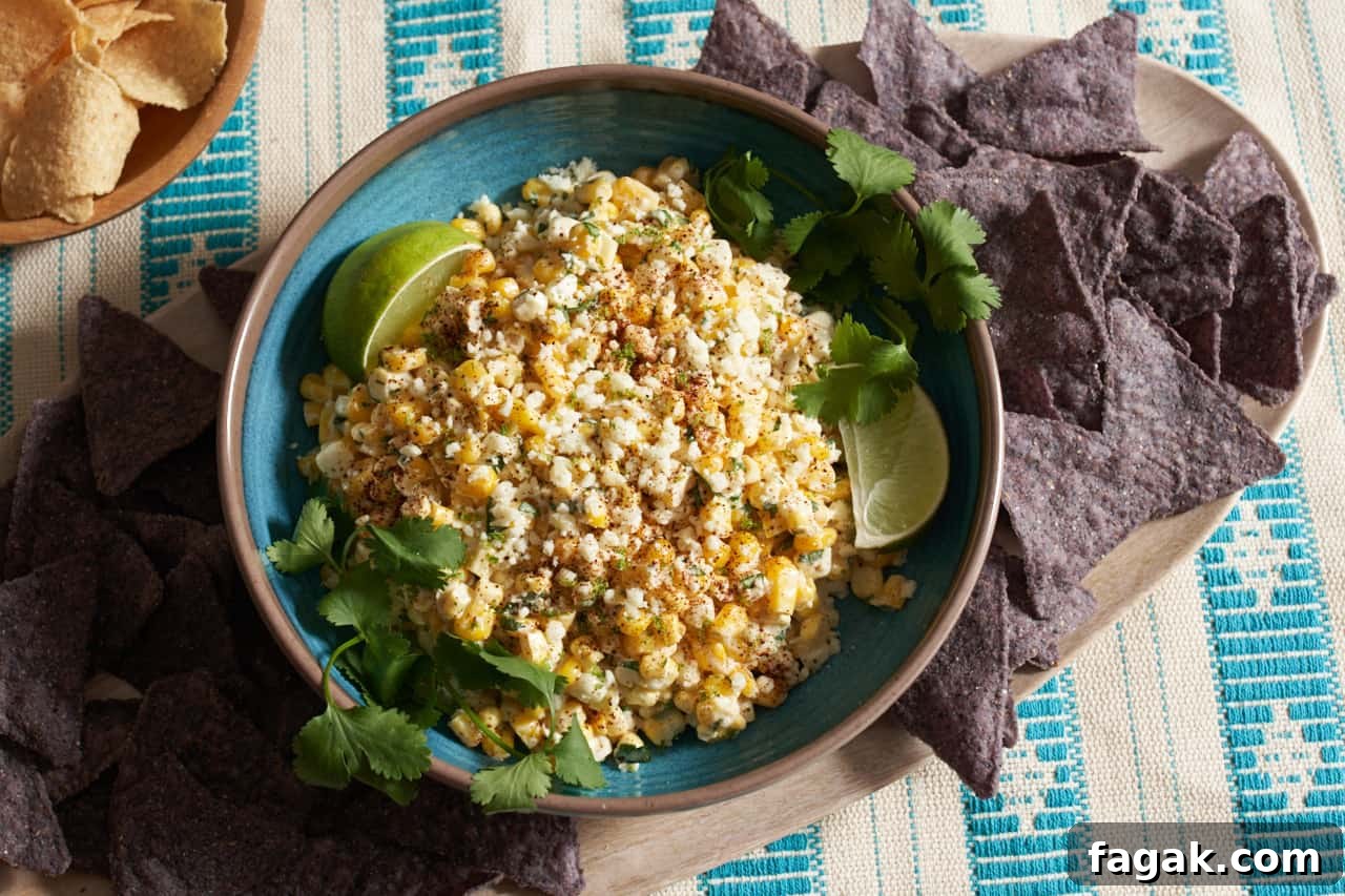 Elote dip in a blue bowl topped with cotija cheese and garnished with lime wedges and fresh cilantro.