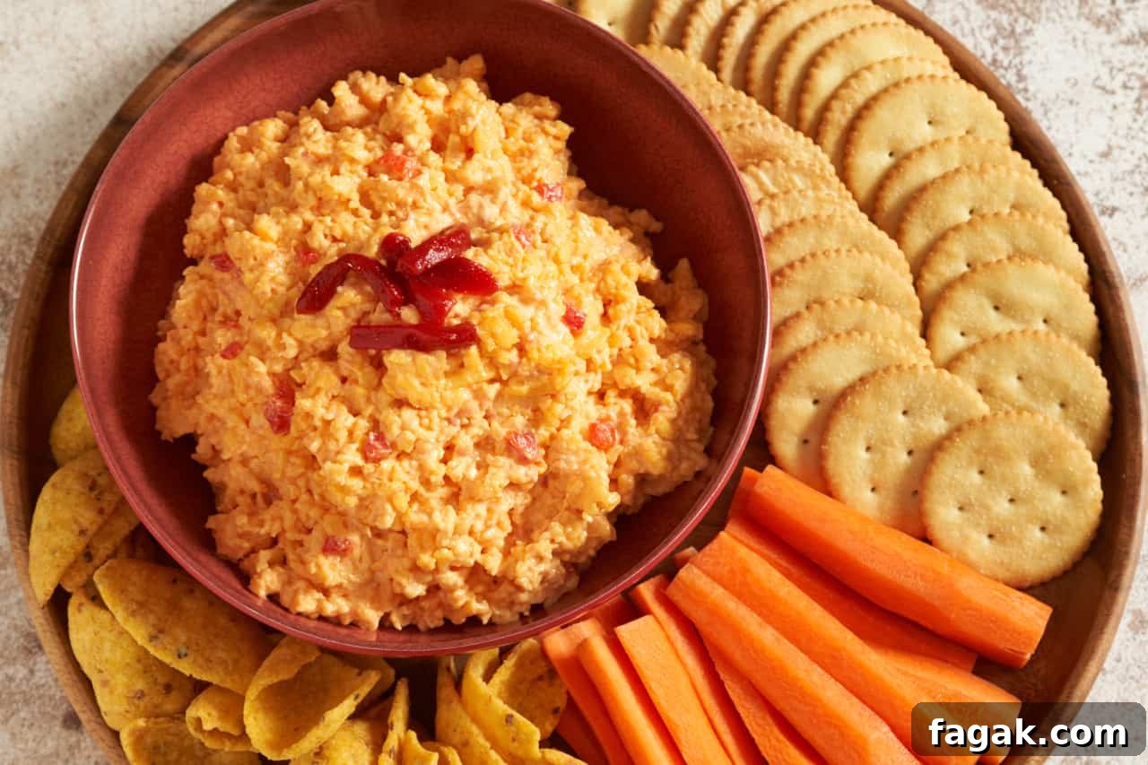 Pimento cheese dip in a red bowl on a round wooden tray.