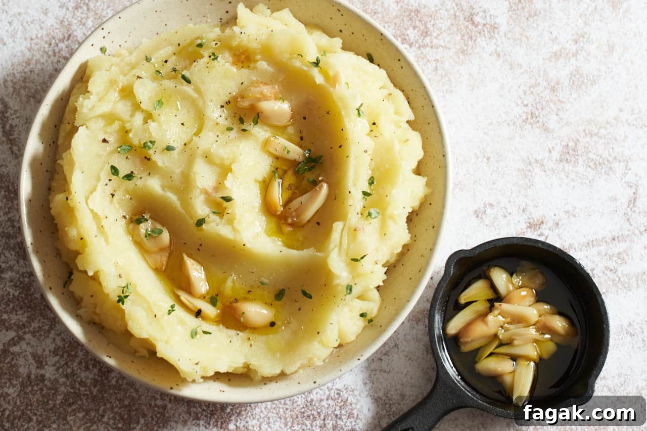 A bowl of mashed potatoes topped with roasted garlic cloves and fresh thyme.