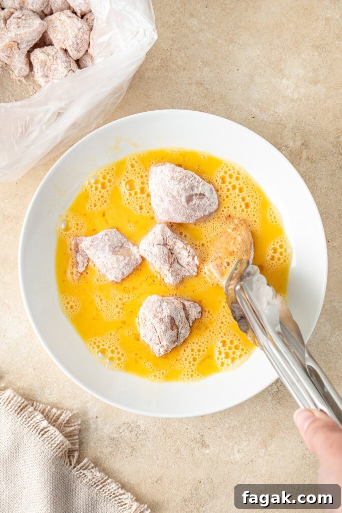 Using tongs to coat the chicken pieces in the egg.