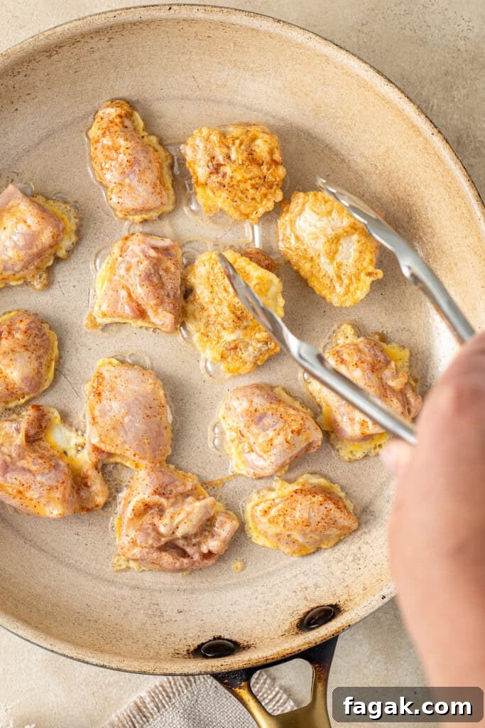 Using tongs to flip the chicken pieces in the frying pan.