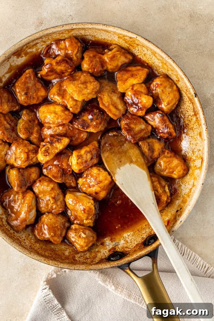 The finished sweet chilli chicken in the frying pan with a wooden spoon.