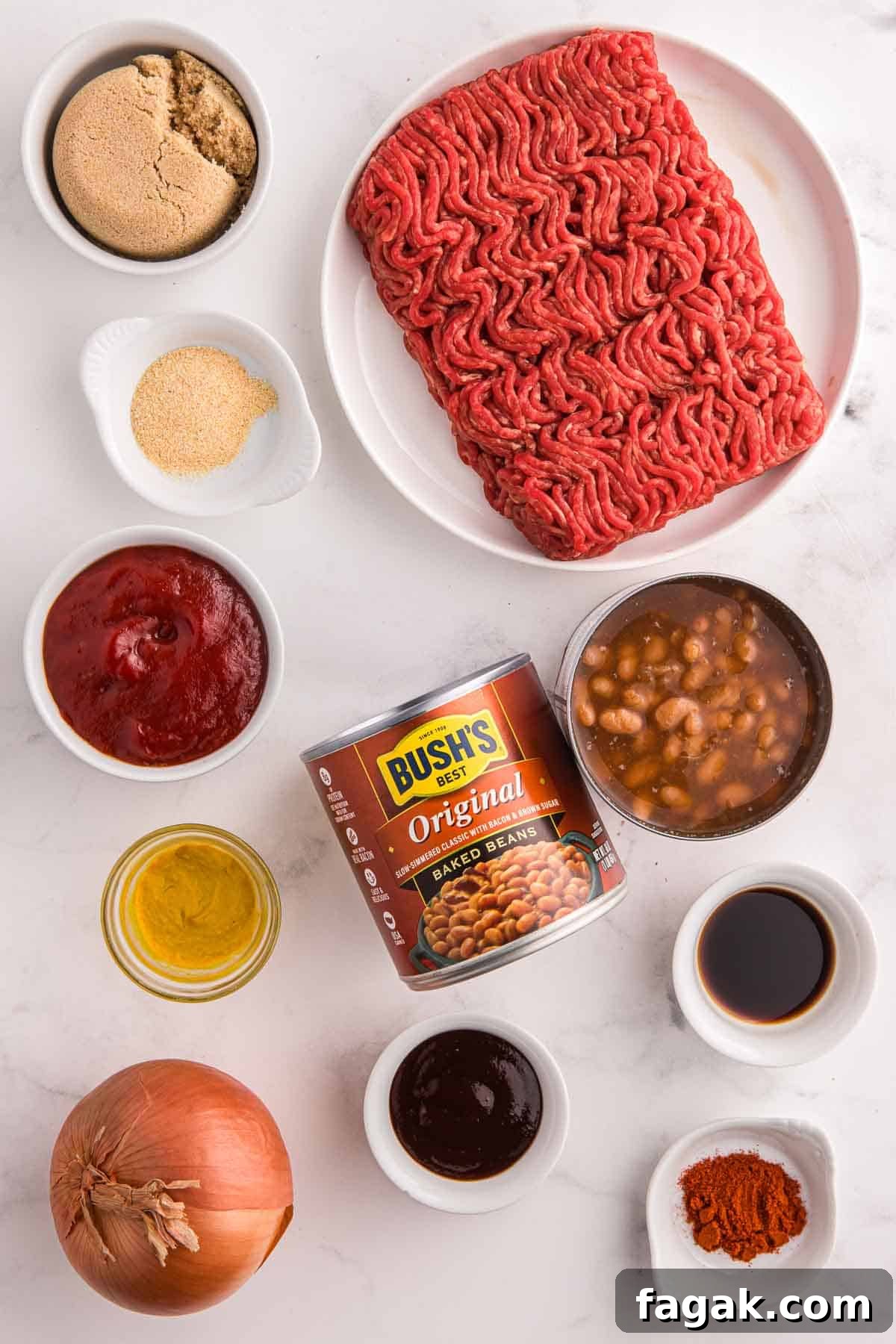 Ingredients arranged for baked beans with ground beef including raw ground beef, diced yellow onion, canned baked beans, brown sugar, ketchup, BBQ sauce, yellow mustard, Worcestershire sauce, smoked paprika, and garlic powder on a light surface.