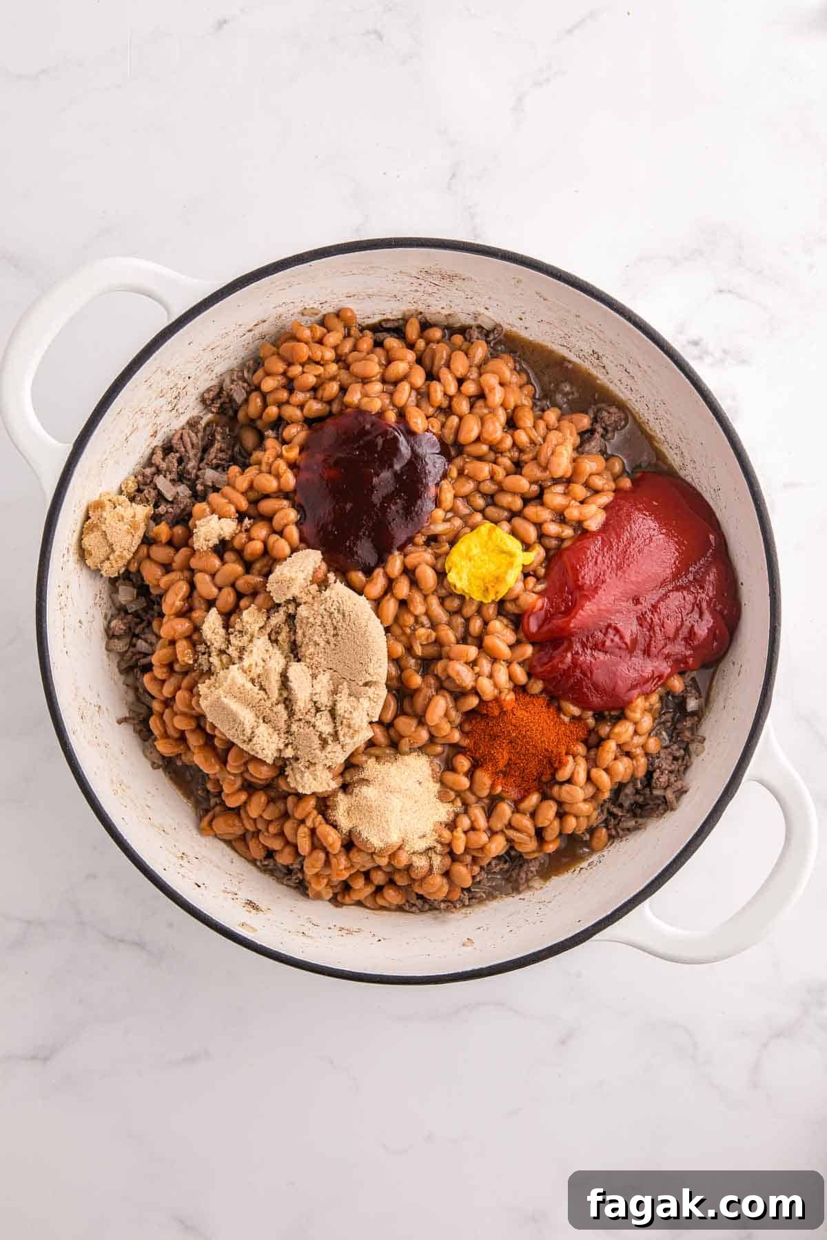 Large pot filled with cooked ground beef, baked beans, brown sugar, ketchup, BBQ sauce, mustard, smoked paprika, garlic powder, and seasonings before stirring. The ingredients are layered together to make baked beans with ground beef.