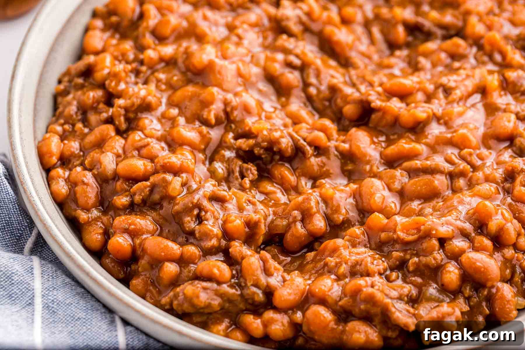 Close up of baked beans with ground beef served in a shallow bowl. The thick sauce coats the beans and beef, giving the dish a rich and hearty appearance.