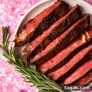Sliced, medium-rare sous vide frozen steak with a dark crust is arranged on a white plate, garnished with fresh rosemary, all set on a bright pink marbled background.