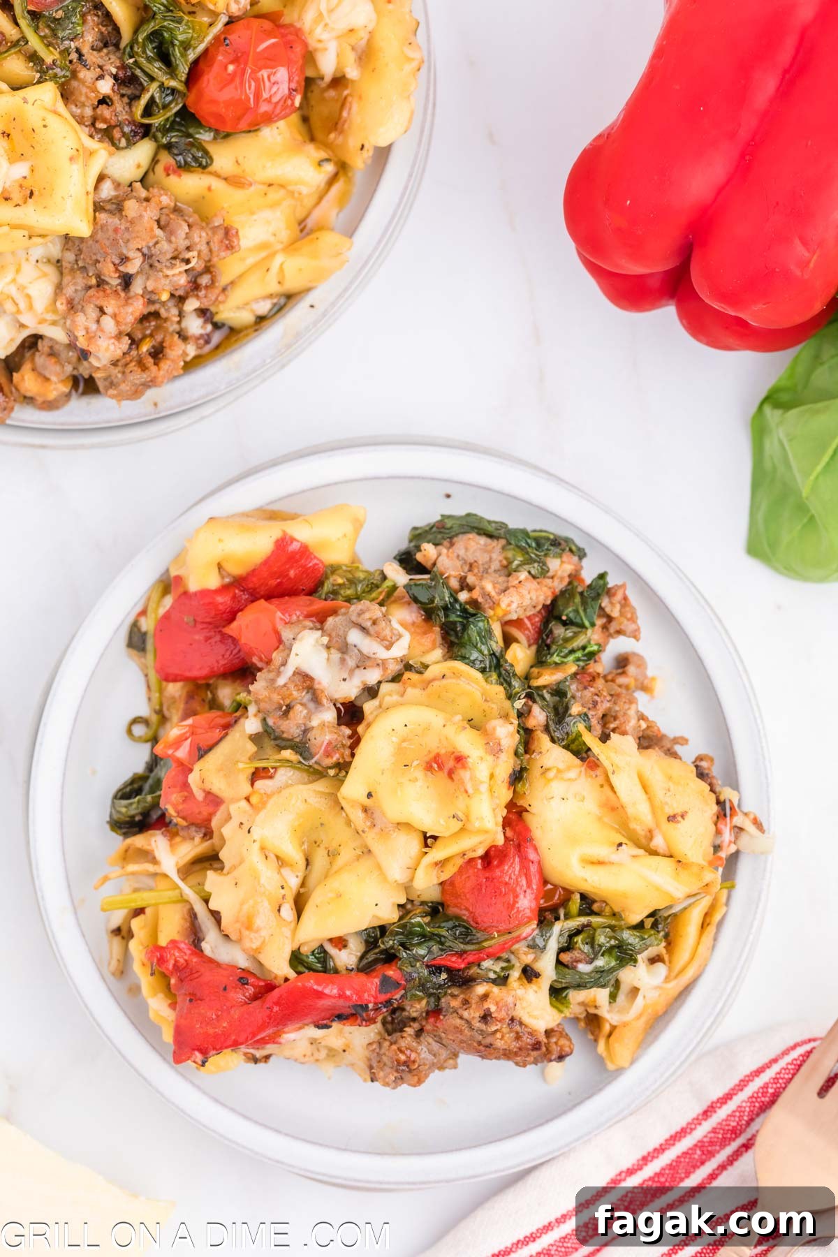 Cooked Tortellini and Sausage on a plate mixed with tomatoes and cooked spinach