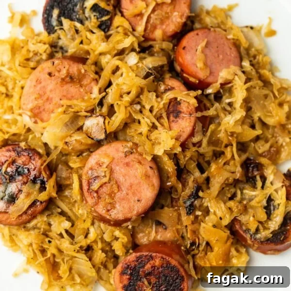 A close-up of cooked sauerkraut mixed with sliced kielbasa and grilled onions on a white plate.