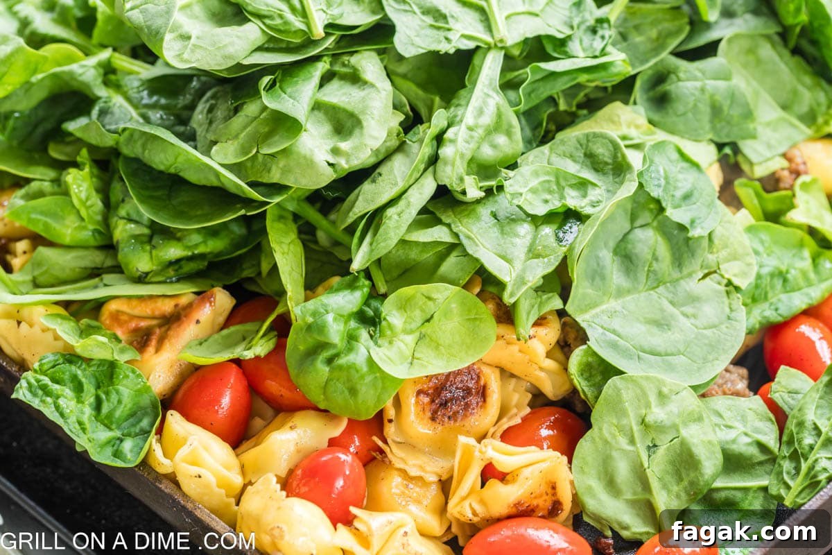 Topping the tortellini and cherry tomatoes with the fresh spinach on the griddle