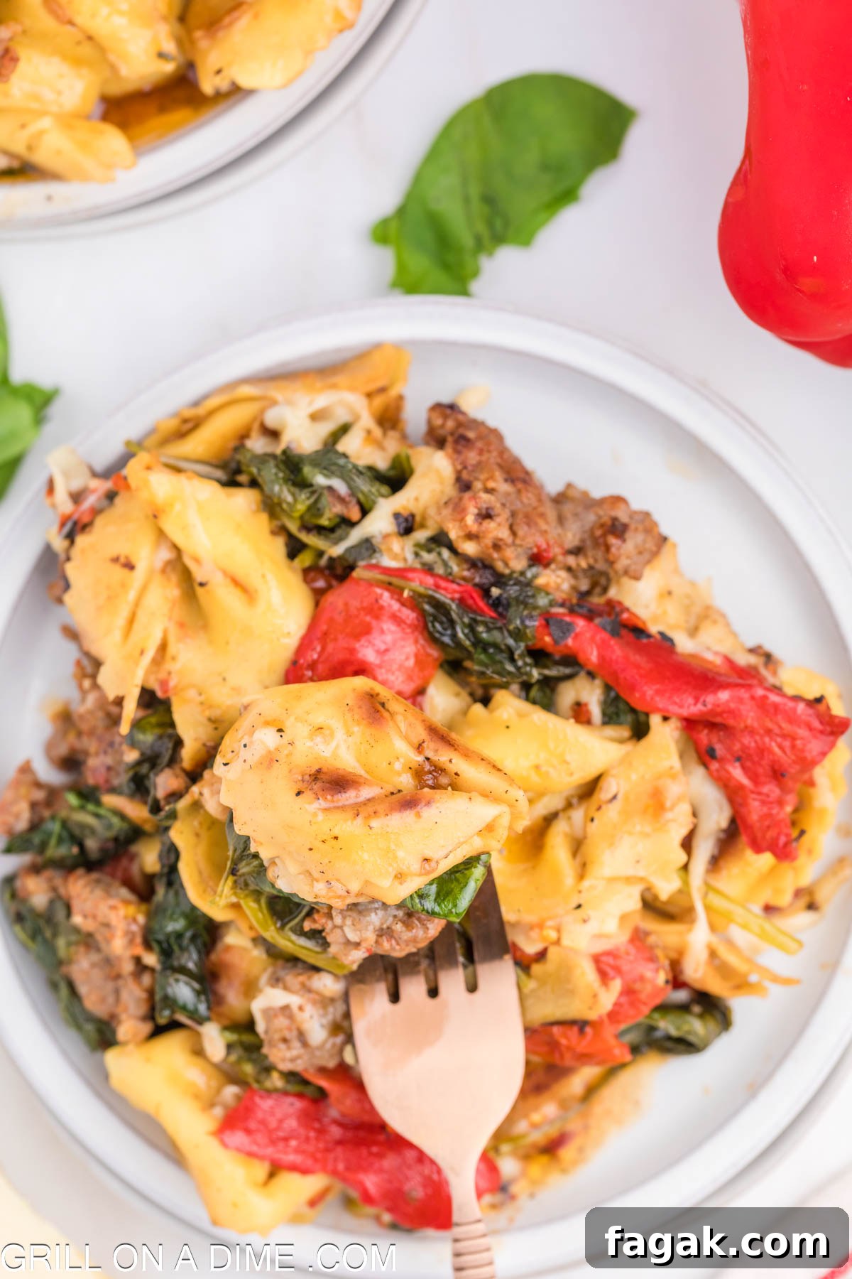 Cooked Tortellini and Sausage, tomatoes, and spinach on a plate with a fork