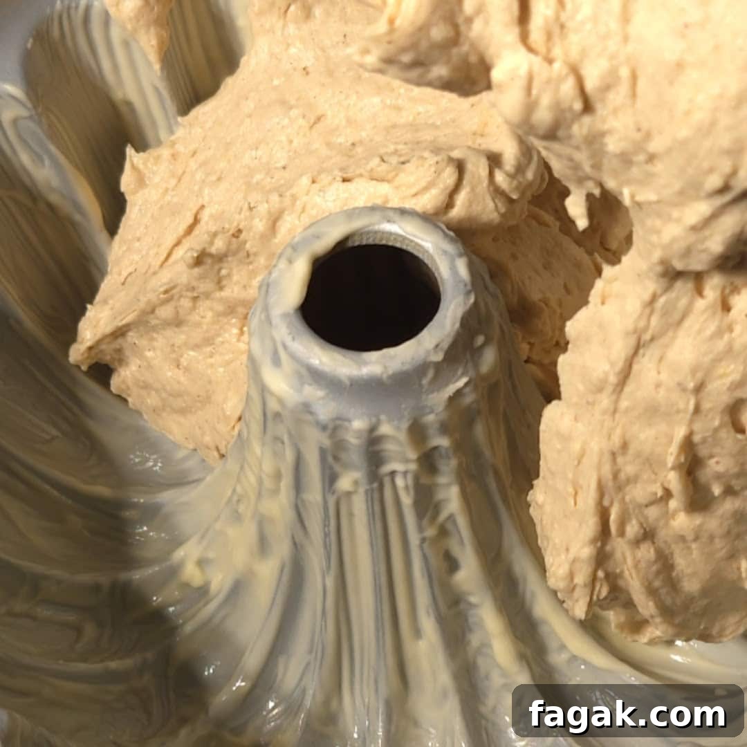 Close-up of the chai cake batter being poured into a greased bundt pan, showcasing its creamy consistency and hint of spices.