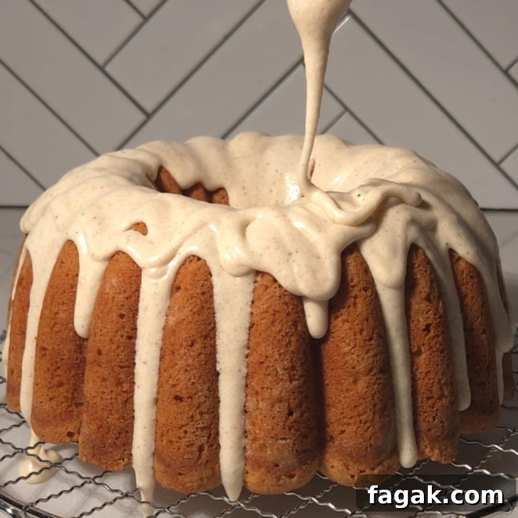 A freshly baked chai bundt cake being drizzled with a thick cream cheese frosting, highlighting the cake's rich spices and moist texture.