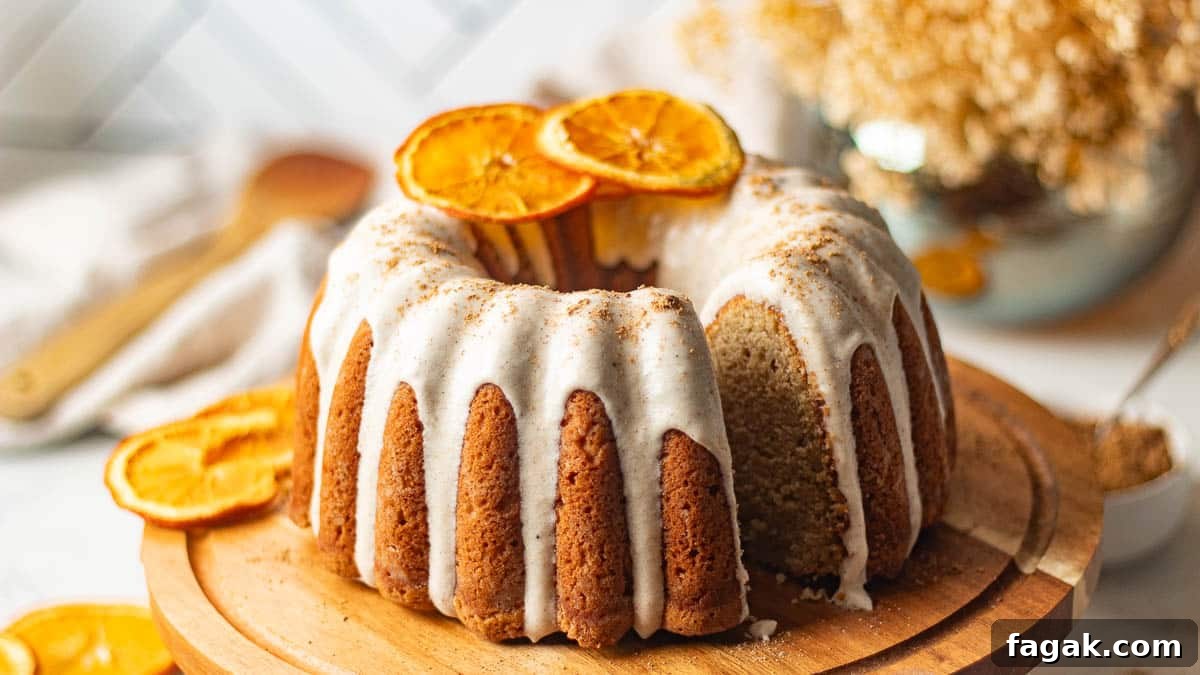 The chai bundt cake presented on a wooden cake stand, frosted with cream cheese icing and garnished with dried orange slices, ready to be served.