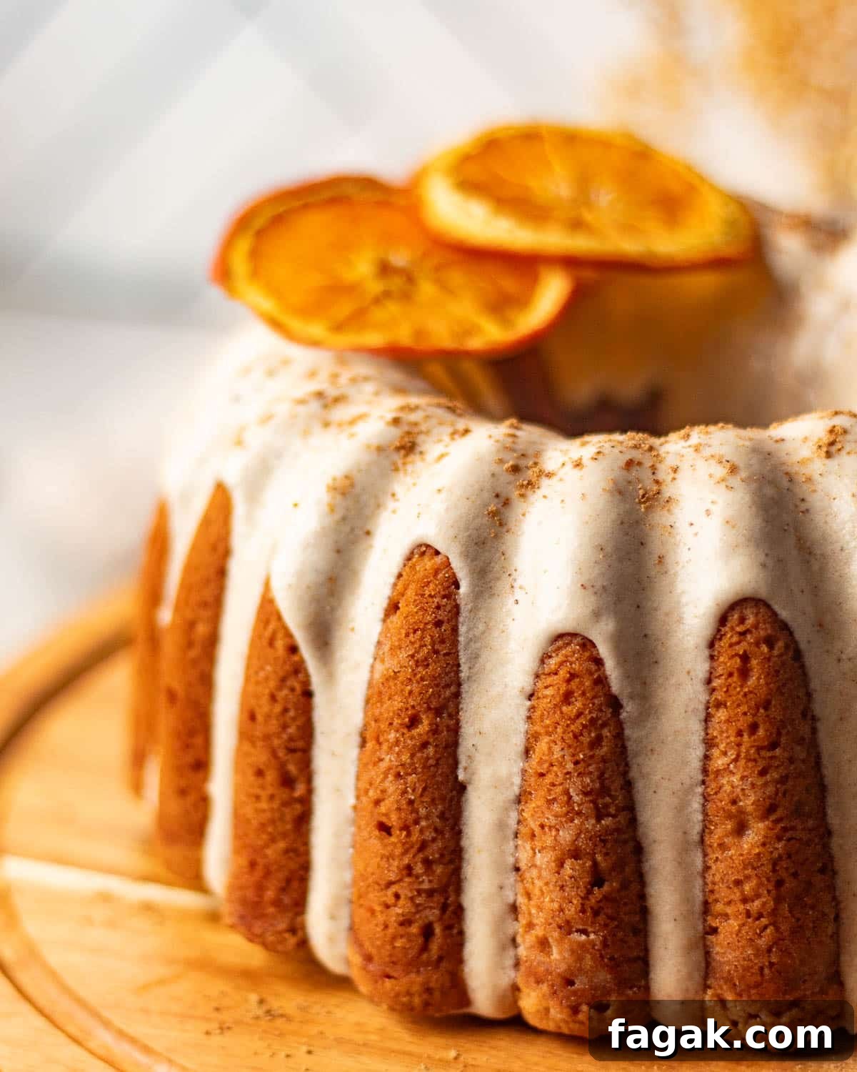 A side view of a chai bundt cake with cream cheese frosting and orange slices, emphasizing the cake's rich, spiced crumb and smooth icing.
