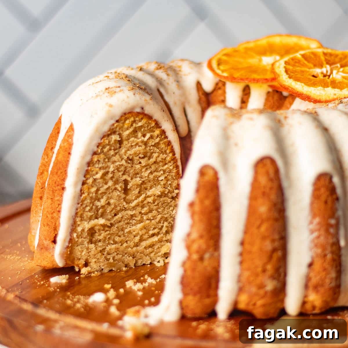 A beautifully frosted chai bundt spice cake with a slice cut out, revealing the soft, spiced interior, topped with dried orange slices for garnish.