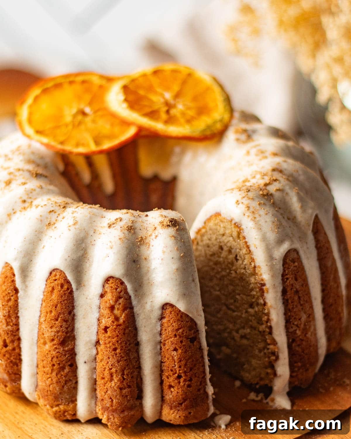 A beautifully presented chai bundt spice cake on a wooden stand, with a slice removed to reveal the soft, spiced crumb inside, highlighting the cream cheese icing and orange garnish.