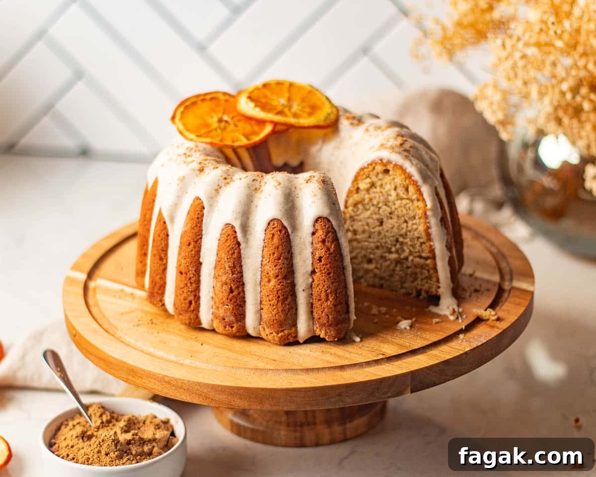 The chai bundt cake presented on a wooden cake stand, frosted with cream cheese icing and garnished with dried orange slices, ready to be served.