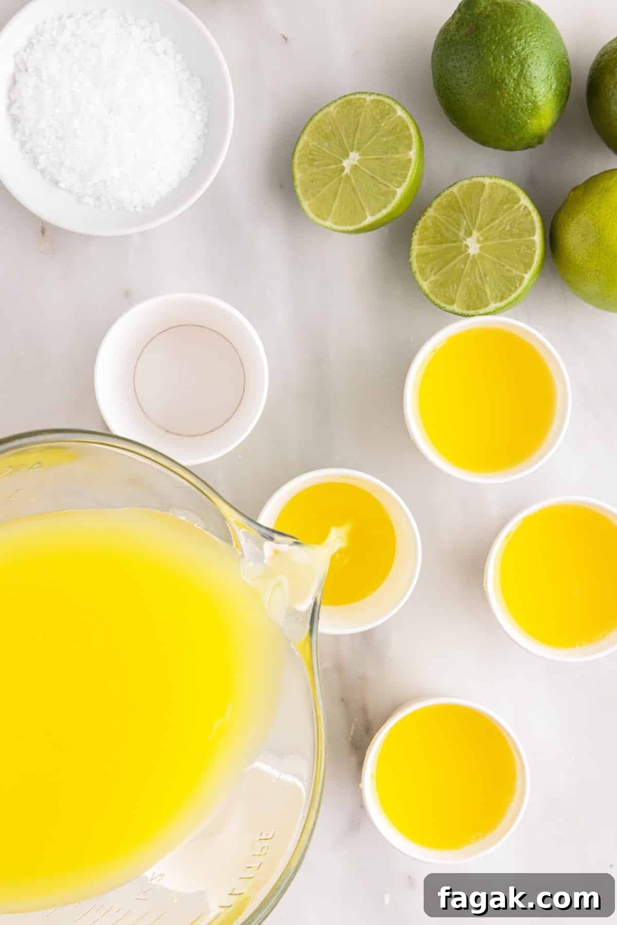Pouring margarita mixture from measuring cup into Dixie cups, limes on table.