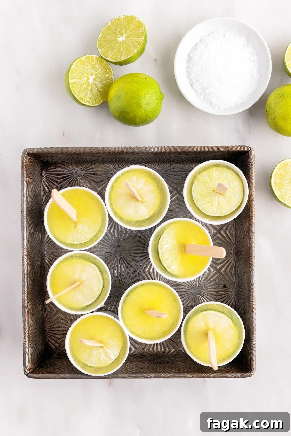 Margarita popsicles set in square cake pan with limes and salt.
