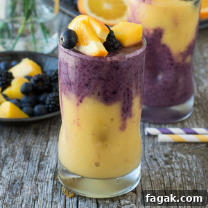 Two glasses of Hawaiian Berry Smoothie, with yellow and purple swirls, are topped with peach slices, blackberries, and blueberries on a rustic wooden surface. A striped straw and plate of fruit complete the vibrant scene.