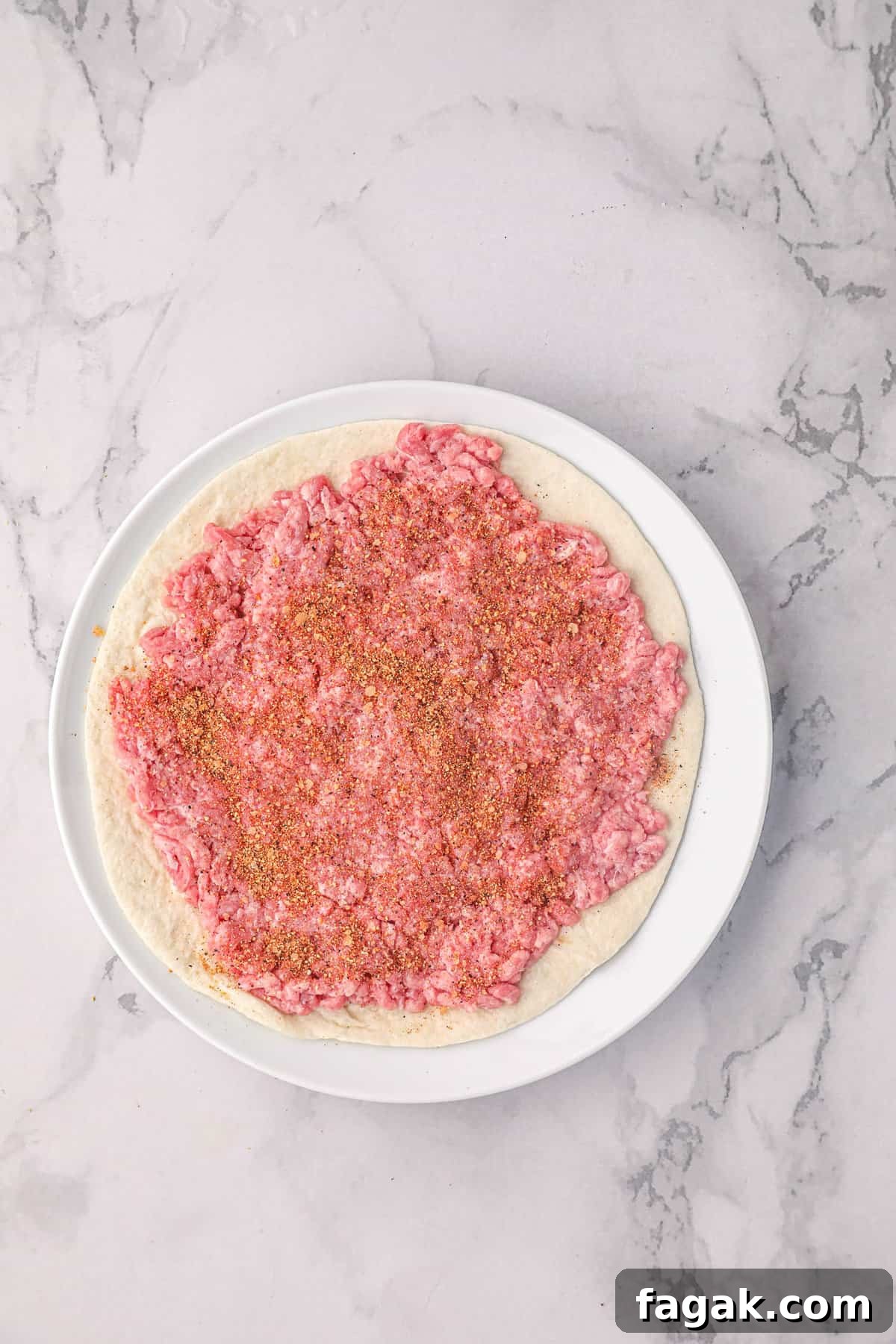Adding beef seasoning to round beef on tortilla for Smash Burger Taco recipe