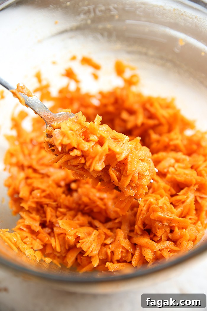 Carrot Kimchi in a glass mixing bowl with a spoon held above from the left with a scoop of carrot kimchi.