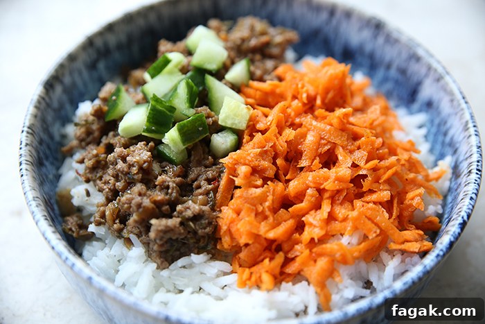 A bowl with white rice with ground beef, diced cucumber, and carrot kimchi.