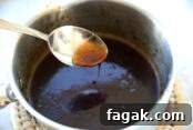 small silver sauce pan with cooked teriyaki sauce in it. There is a spoon dipped in to show the consistency of the sauce