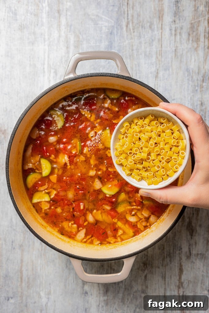 A small bowl of ditali pasta held over a pot of minestrone soup.
