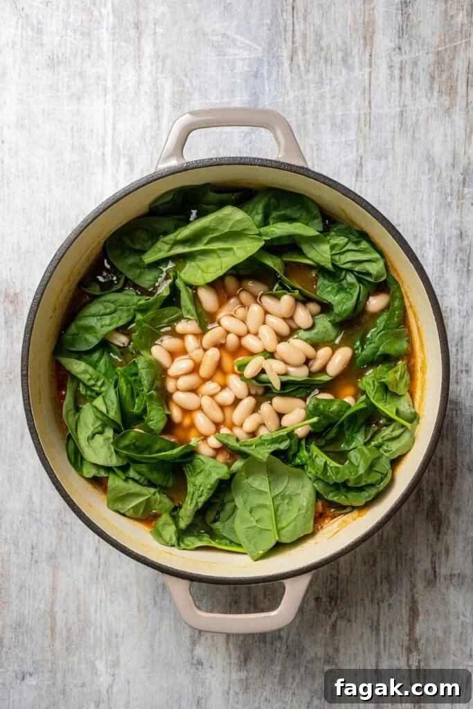 Cannellini beans and baby spinach leaves added to a pot of minestrone soup.
