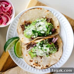 Slow-Braised Chuck Roast Tacos with Salsa Verde 9 Roast tacos on a white plate with lime slices.
