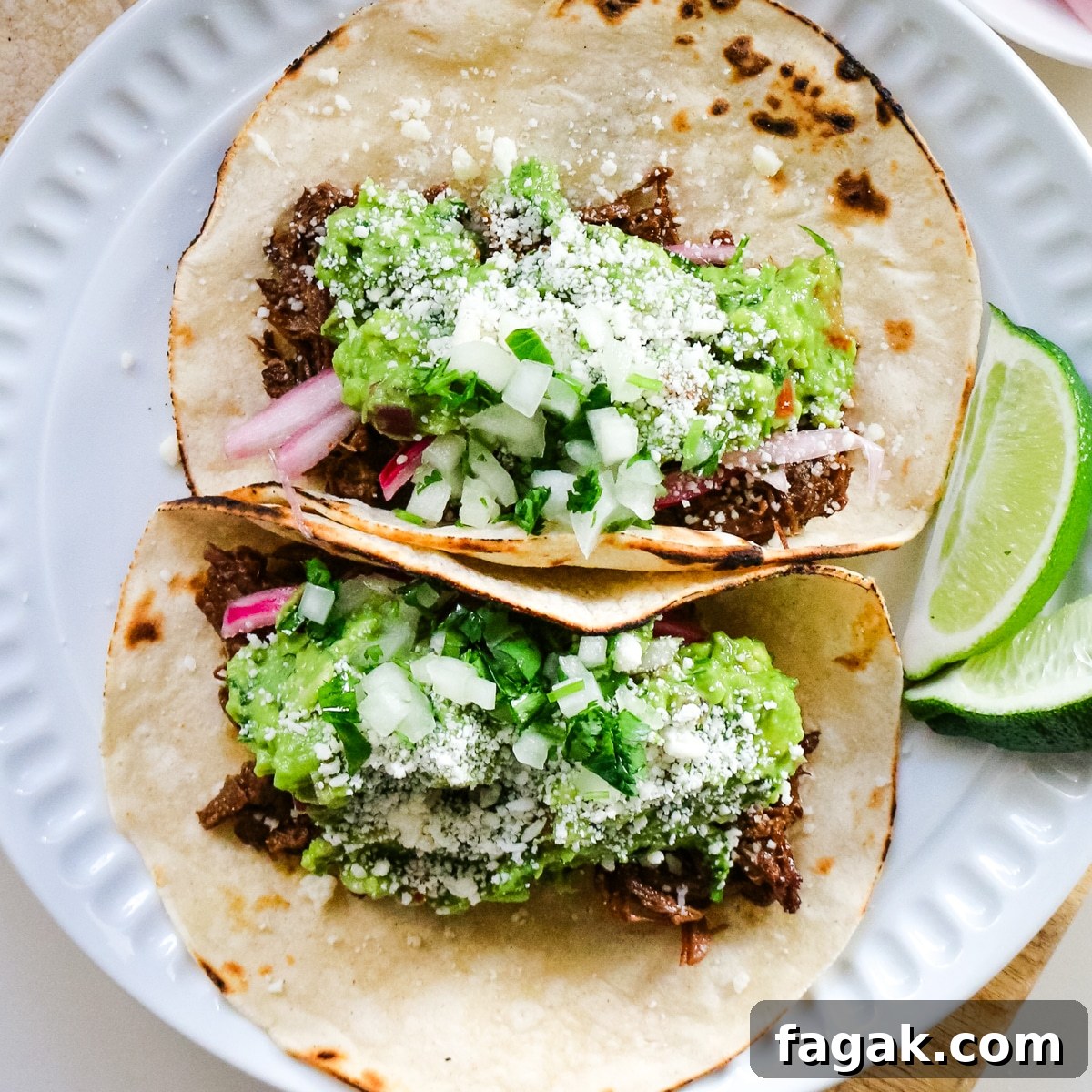 Slow-Braised Chuck Roast Tacos with Salsa Verde 7 Roast tacos on a white plate with lime slices.