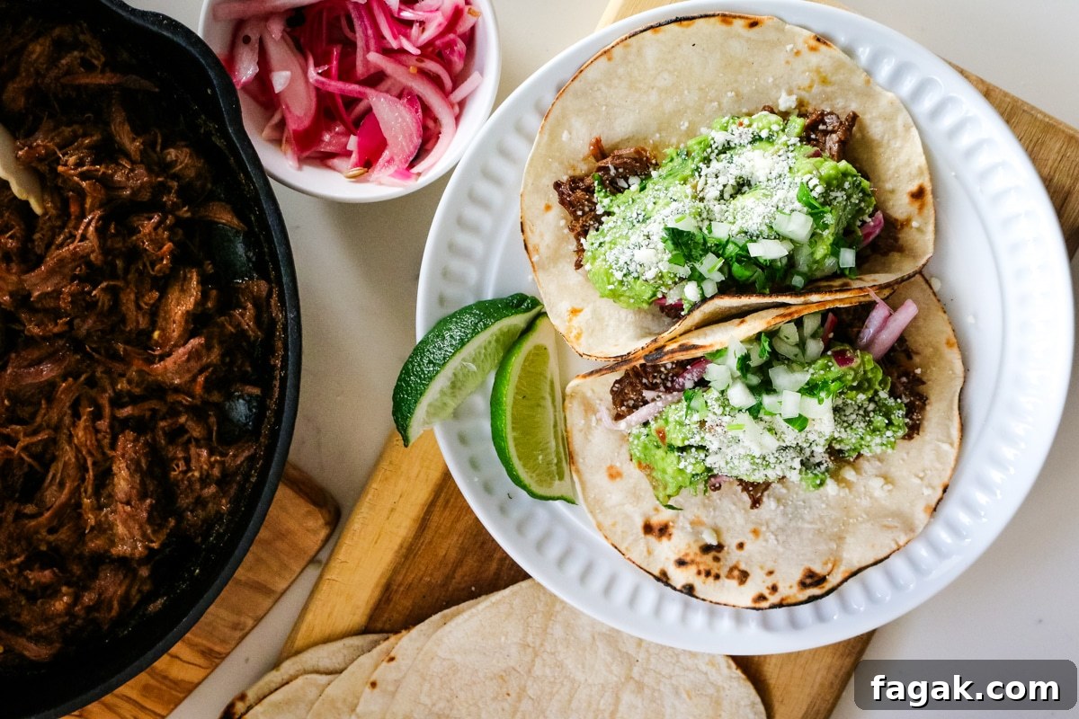 Slow-Braised Chuck Roast Tacos with Salsa Verde 8 Roast tacos on a white plate with roasted beef in a pan, with tacos and onions beside it.