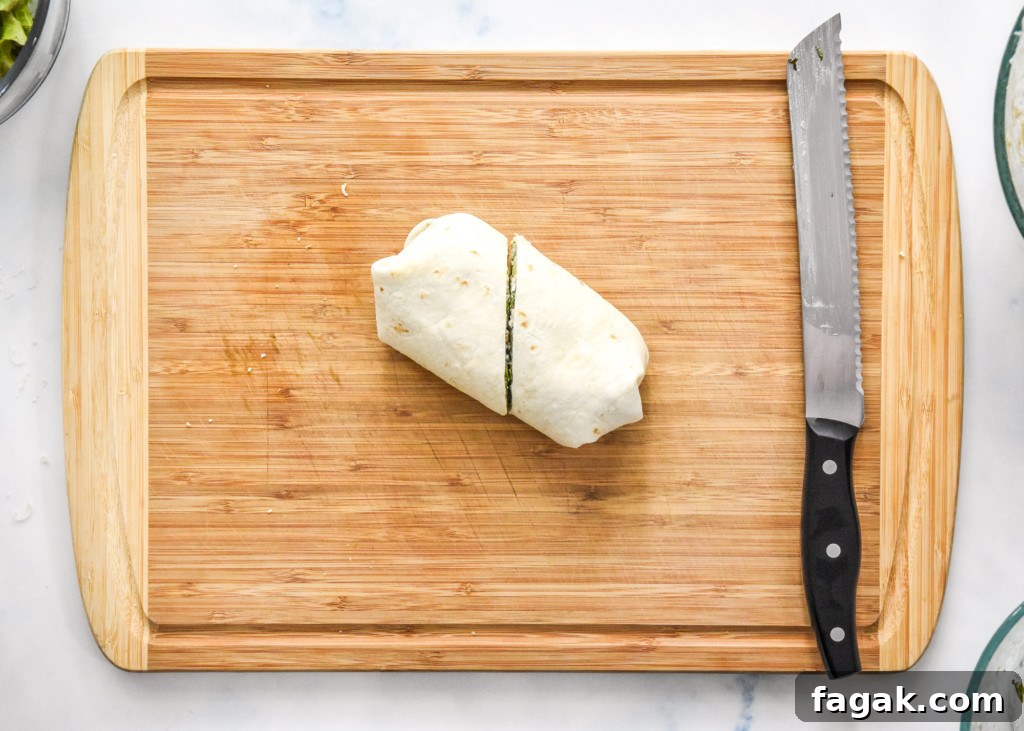 prepared caesar chicken salad lunch wrap cut in half on a cutting board.