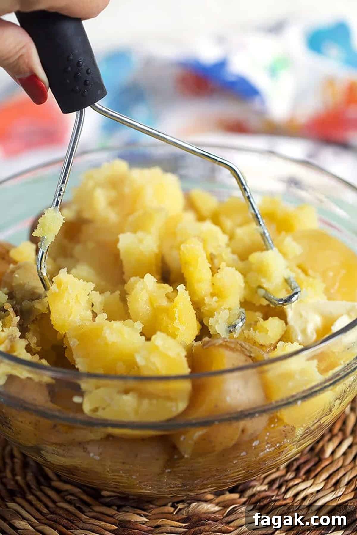 Potatoes being mashed with a potato masher in a glass bowl